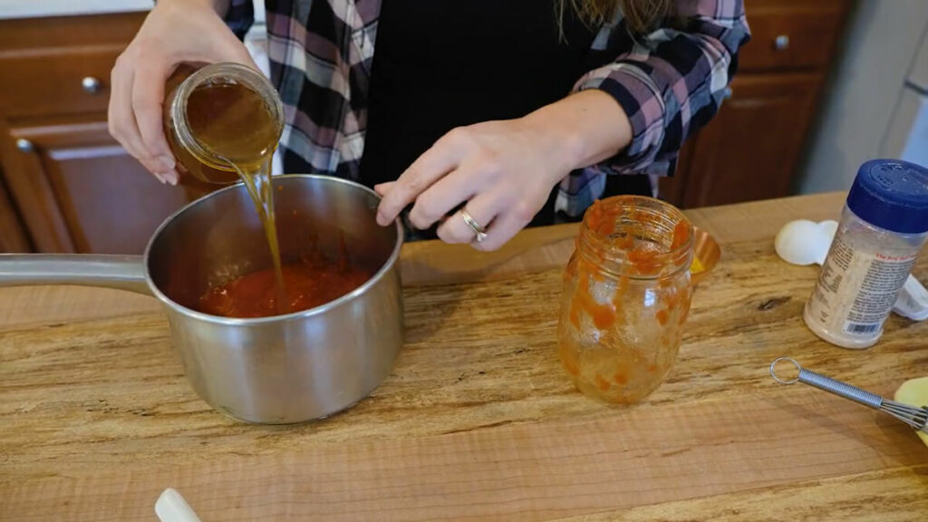 Pouring a jar of bone broth into a pot with tomato sauce.