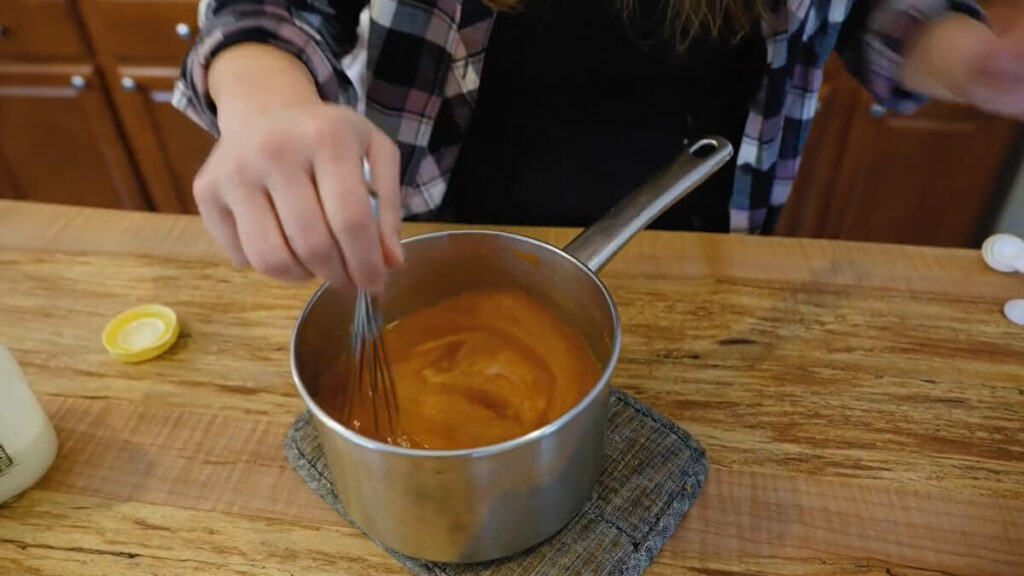 A woman's hands whisking cream into a pot of tomato soup.