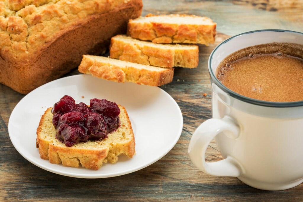 Sliced gluten free bread on a white plate with jelly. Cup of coffee and sliced bread in the background.
