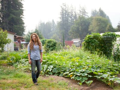 A woman standing in front of a large vegetable garden.