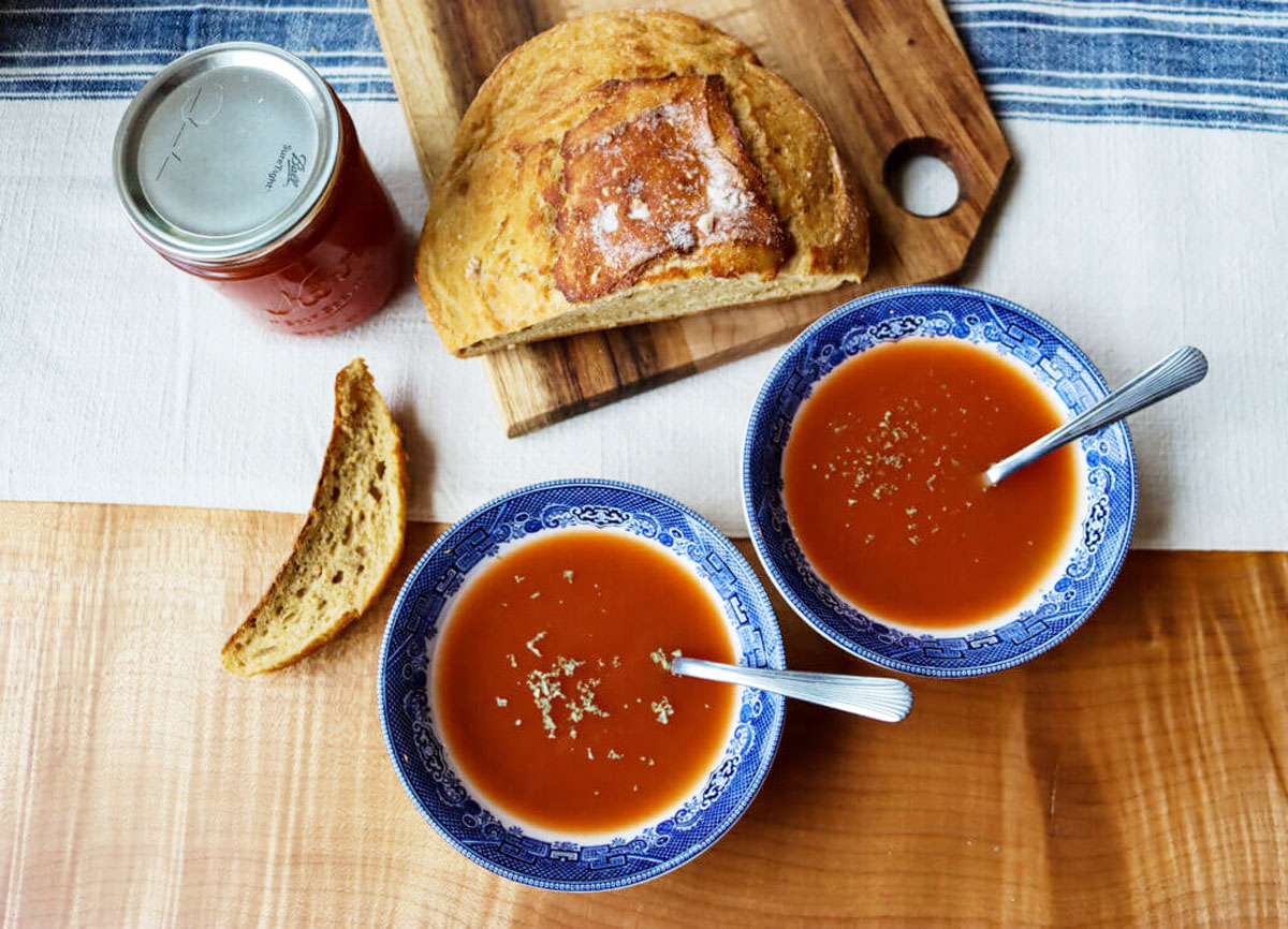 Two bowls of tomato soup with a loaf of bread and a jar of tomato sauce beside it.