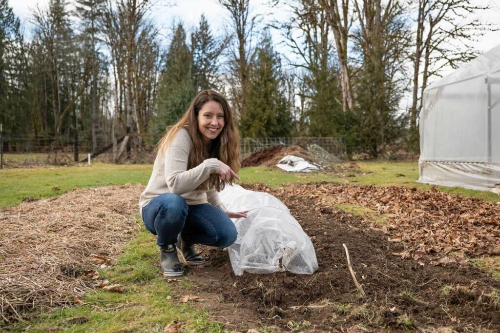 A woman crouched down pointing at a polytunnel in her garden.