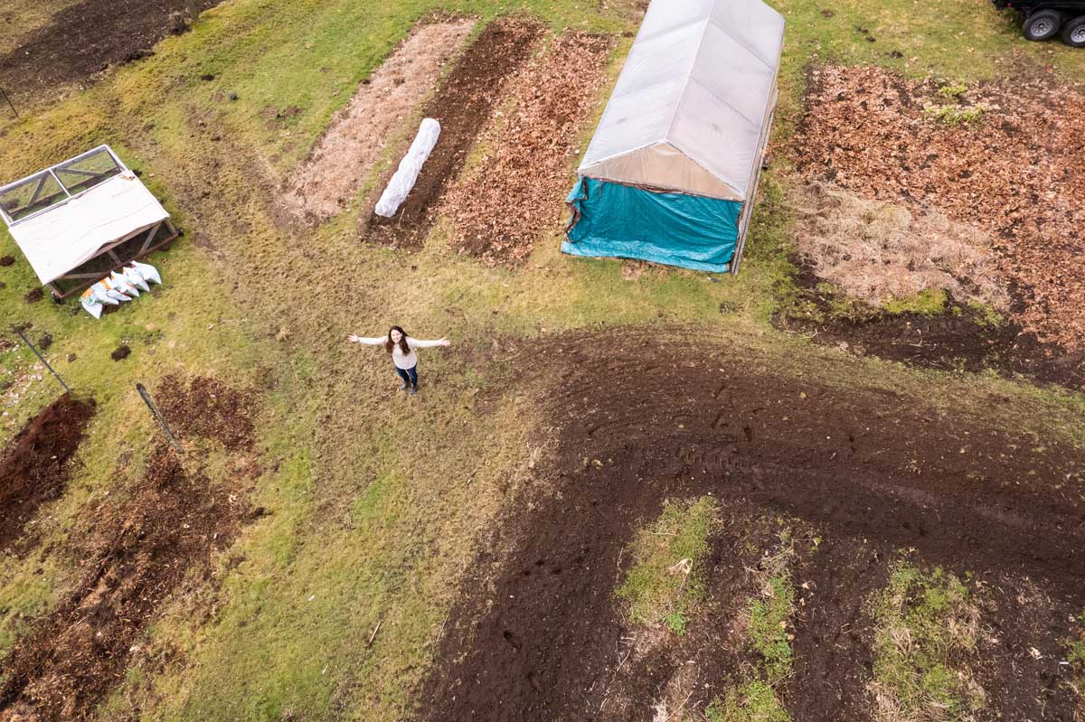 A shot of a homestead property from a drone up high with a woman standing arms out in the center.