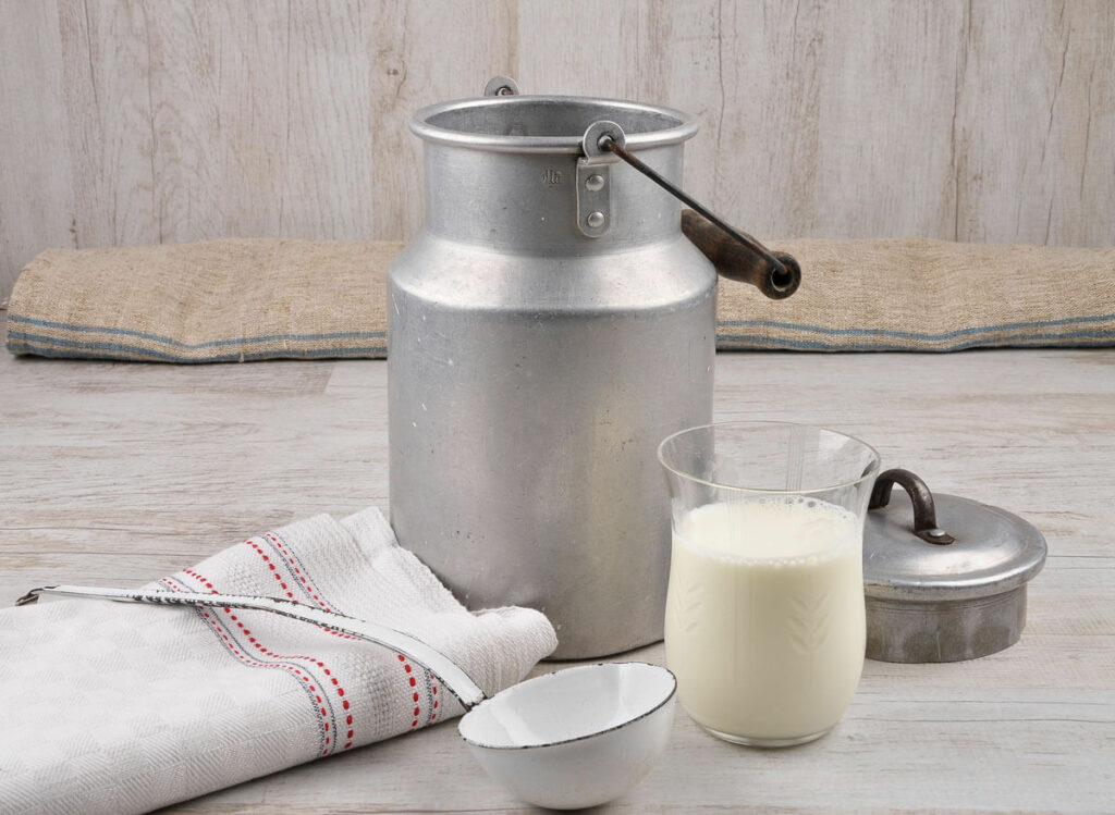 Old fashioned milk jug next to a glass of milk.