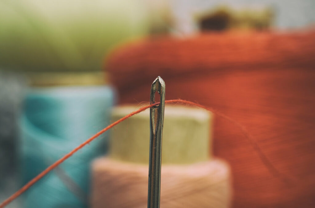 Needle and old fashioned spools of thread behind it.