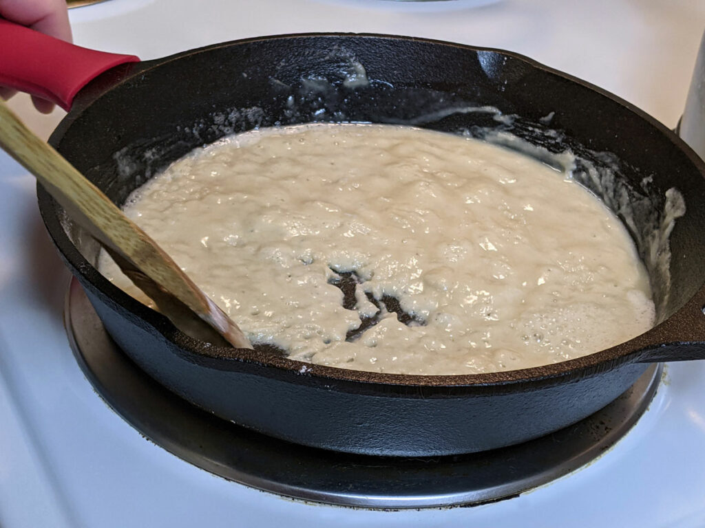 Cast iron skillet with roux being stirred with a wooden spoon.