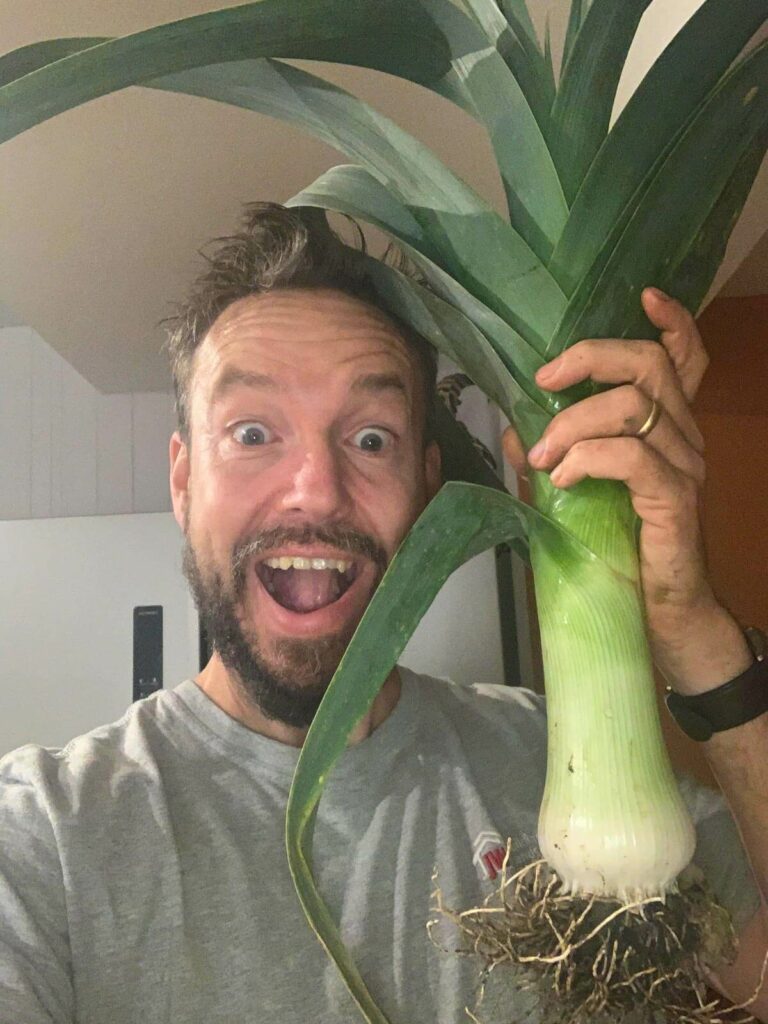 A man holding up a large leek.