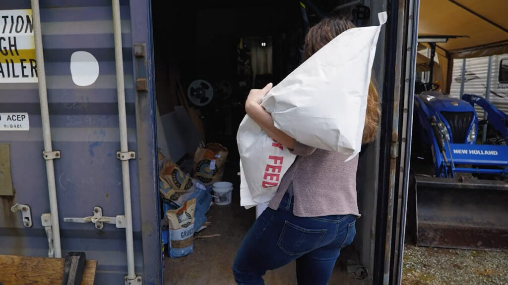 A woman hauling a bag of pig feed.