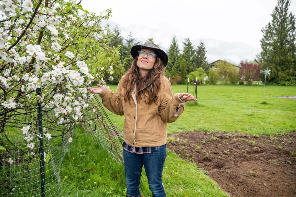 A woman standing by a flowering apple tree while it rains.