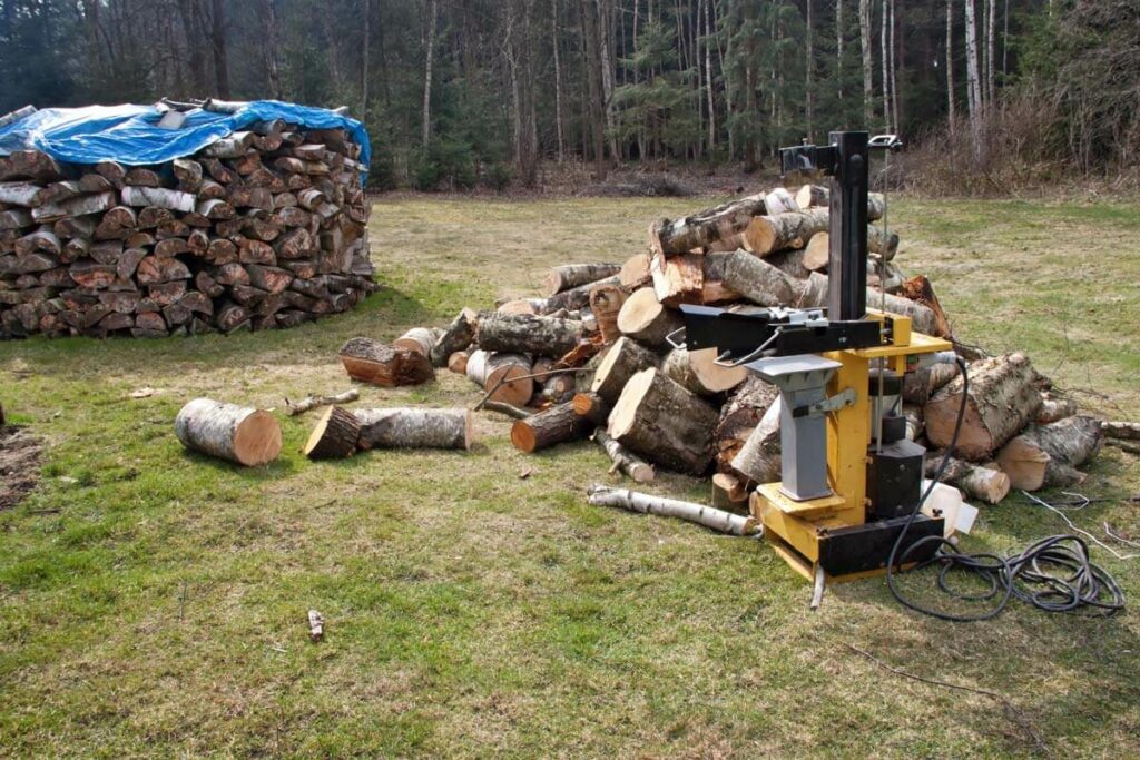 Wood splitter in a field with a large stack of wood.