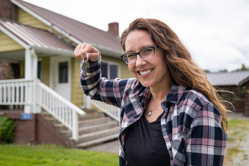 A woman holding keys with a yellow house in the background.