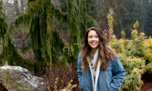 A woman sitting on a rock beside an herb garden.