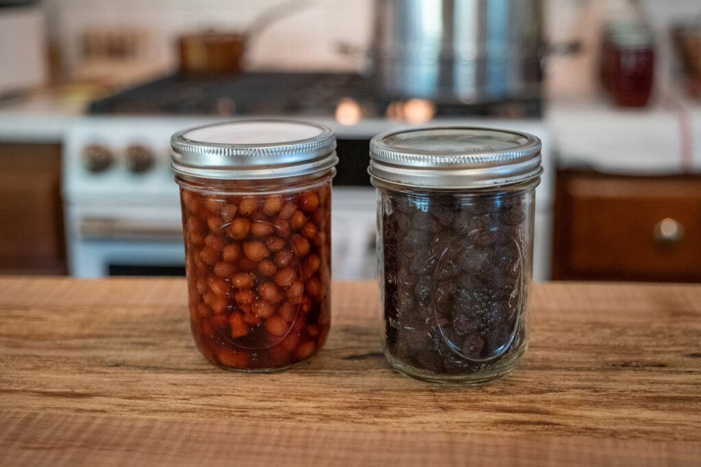 A jar of dehydrated cherries and fruit vinegar on a wooden countertop.