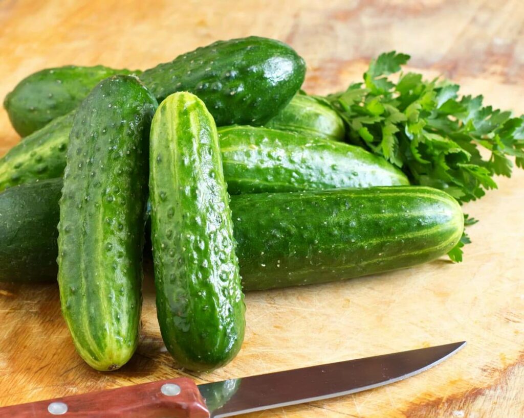 Cucumbers piled on a cutting board with a knife next to them.