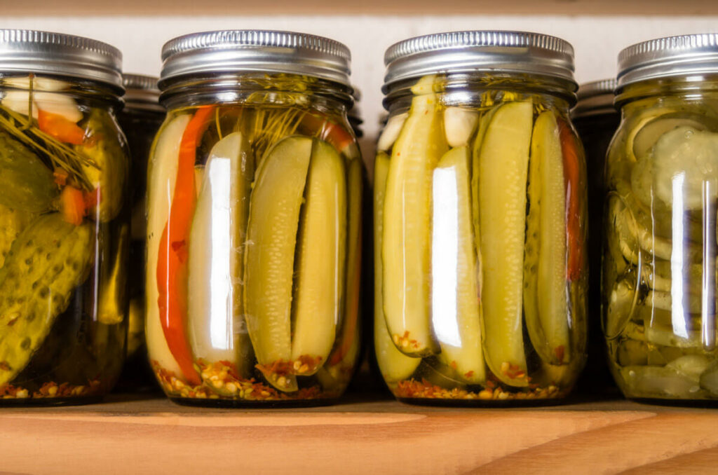 Different kinds of canned pickles on a pantry shelf.