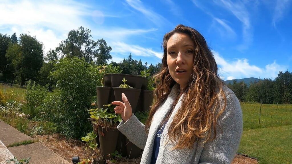 A woman pointing to strawberries growing in a vertical tower garden.