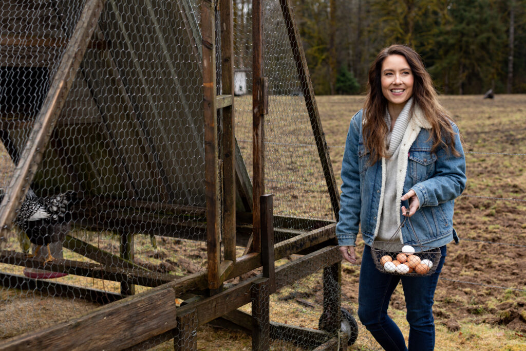 A woman standing beside a chicken coop with a basket full of fresh eggs.