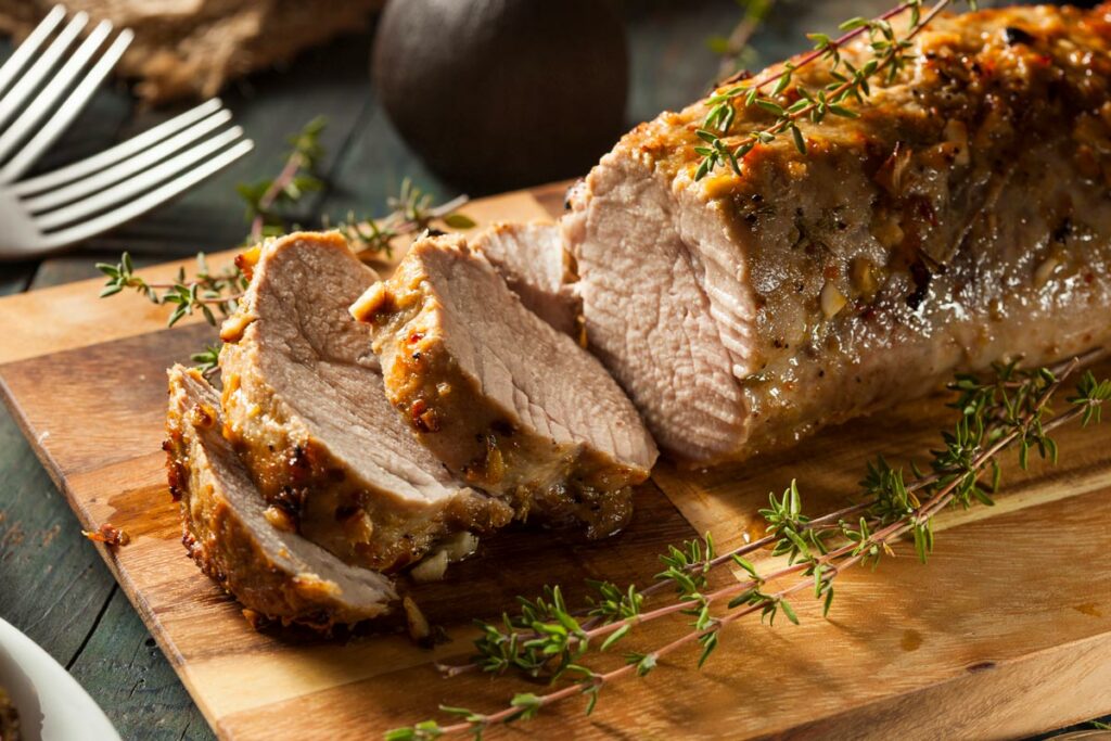 A pork tenderloin cooked and sliced on a wooden cutting board.