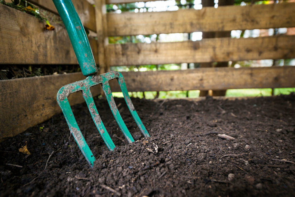 Finished compost in a wooden bin with a blue pitchfork.