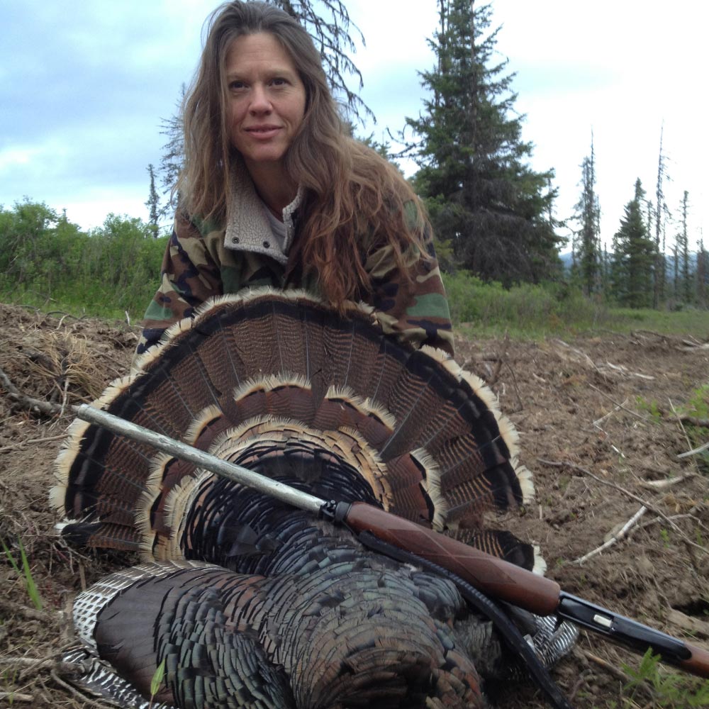 Image of a woman holding a turkey with a rifle laying against it.