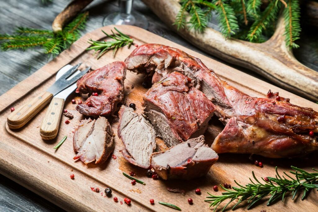 Wild game meat cooked and sliced on a wooden cutting board.