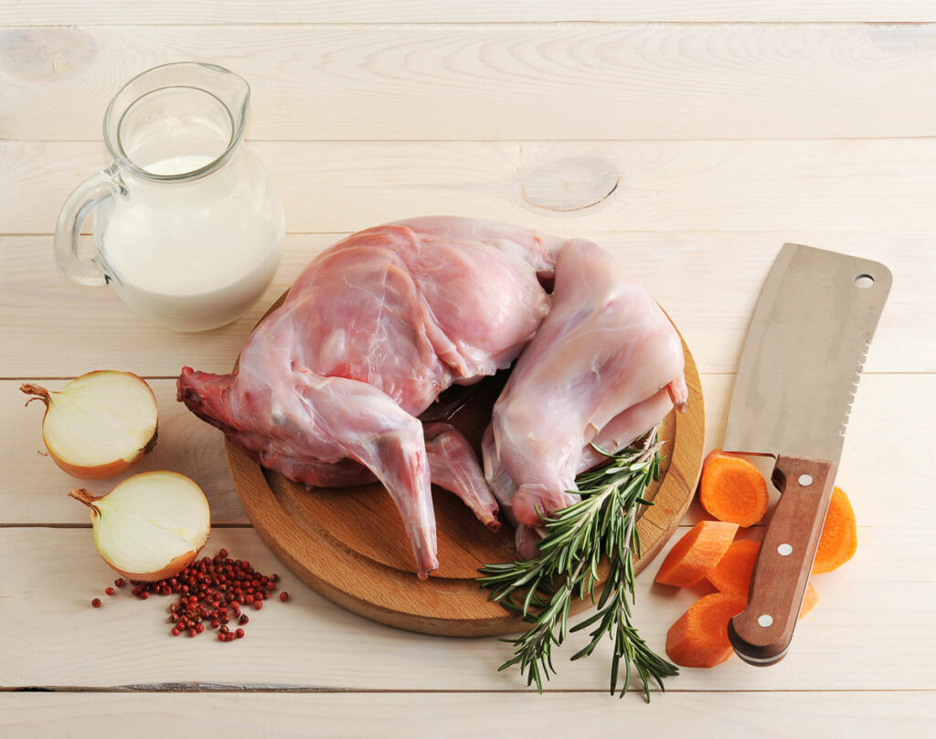 Rabbit on a cutting board with herbs and spices on the table.