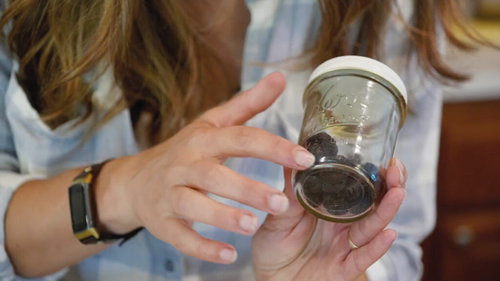 Dehydrated cherries in a jar with a woman's hand pointing to them.