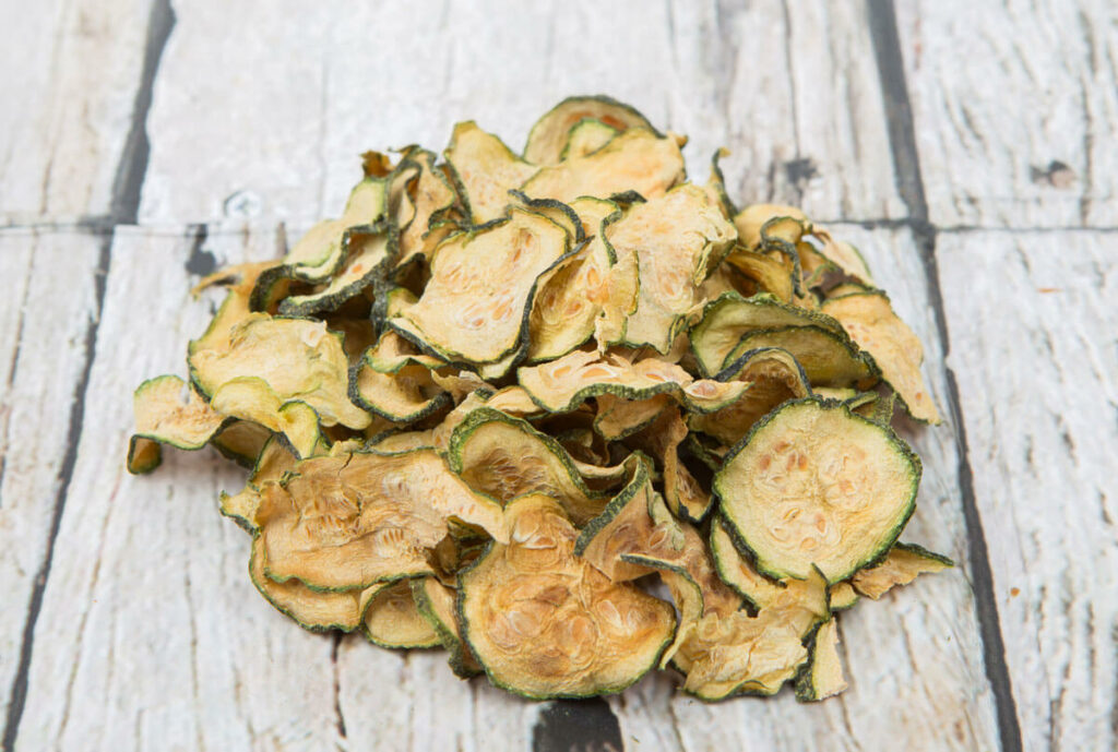 Dehydrated zucchini chips on a wooden backdrop.