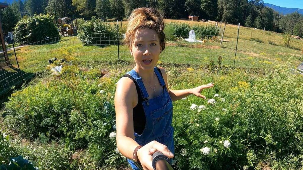 A woman holding a camera standing in her garden.