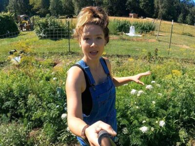 A woman holding a camera standing in her garden.
