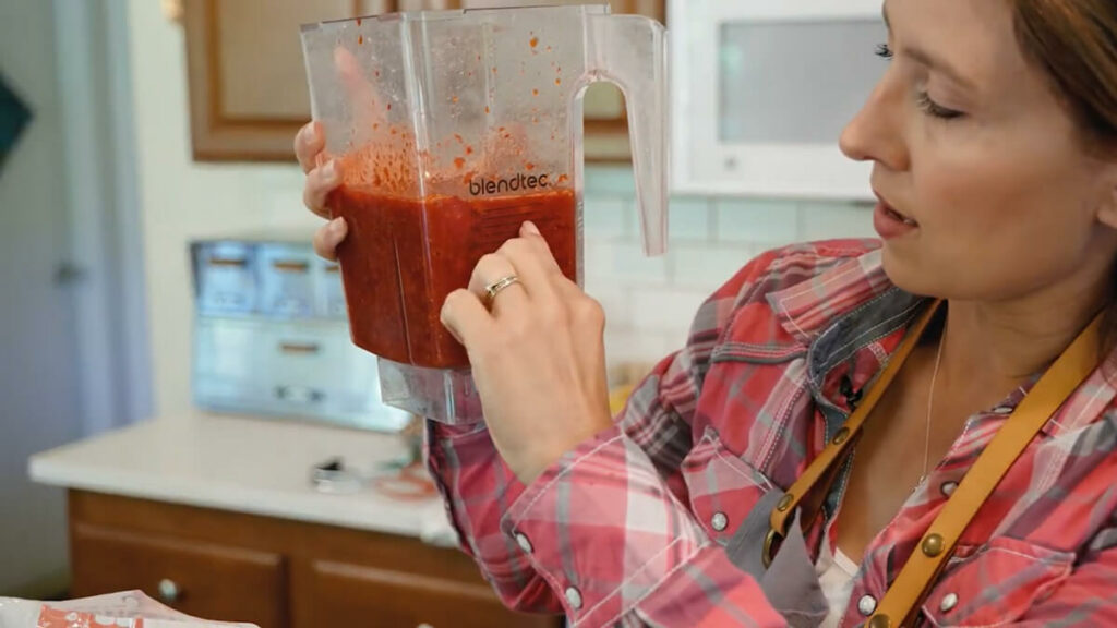 A woman holding a blender with blended strawberries.