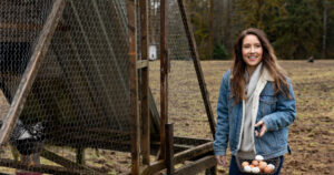 A woman standing beside a chicken coop with a basket full of fresh eggs.