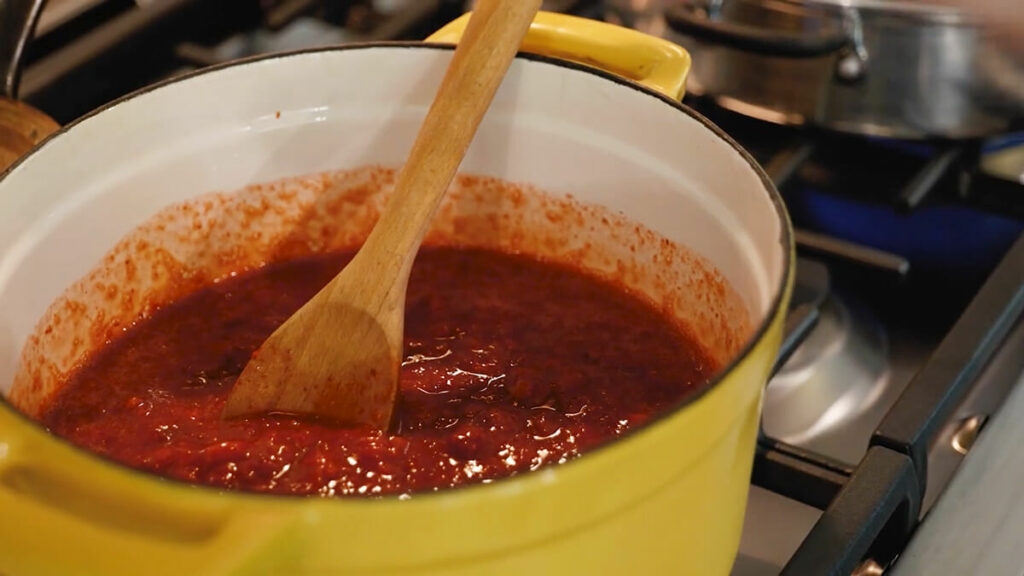 Strawberry jam cooking in a yellow pot on the stove.