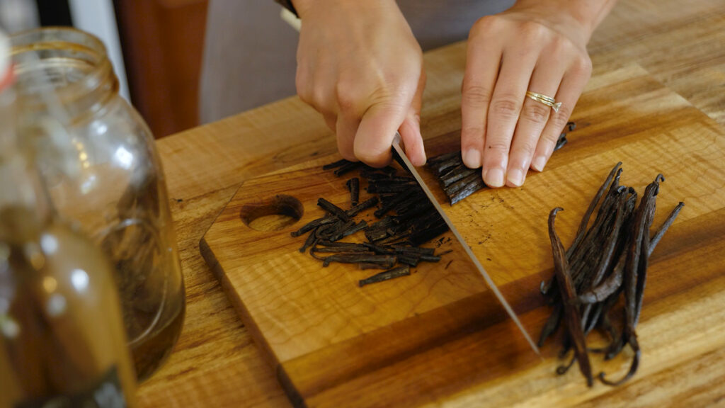 Woman's hands cutting vanilla beans on a wooden cutting board.