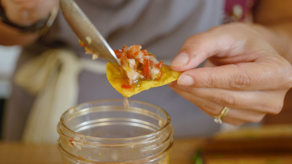 A woman's hands spooning fermented salsa onto a tortilla chip.