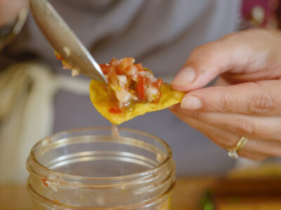 A woman's hands spooning fermented salsa onto a tortilla chip.