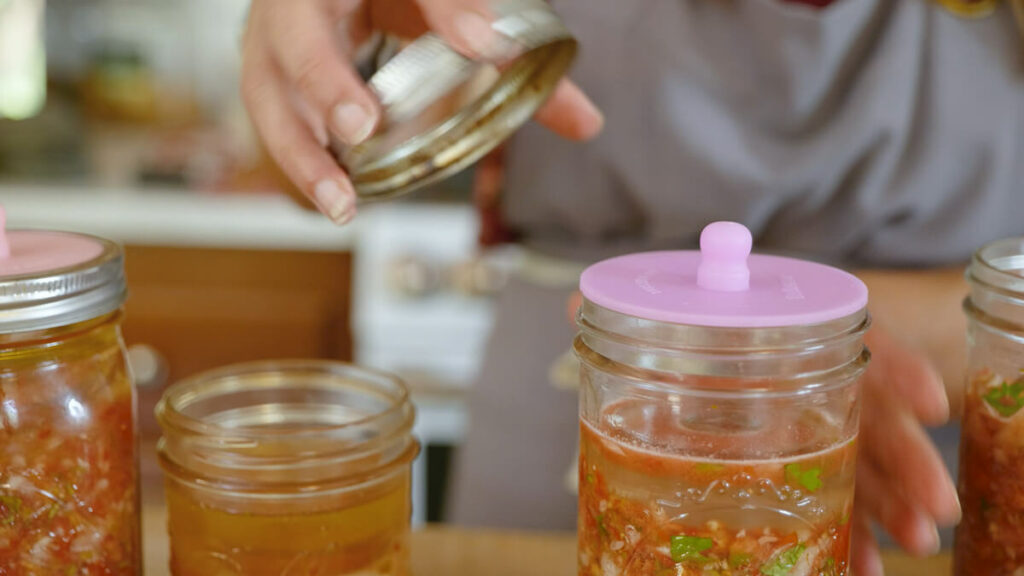 Adding a fermenting lid to a Mason jar of salsa.