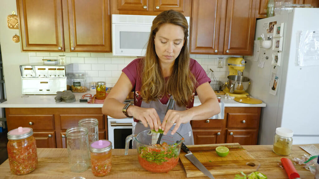 A woman squeezing fresh lime juice into a bowl of fresh salsa.