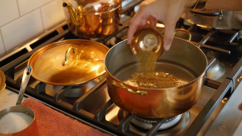 Adding mustard seed into a pot of pickle brine.