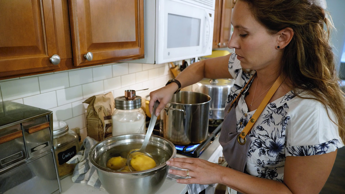 A woman placing blanched pears into a bowl of water.