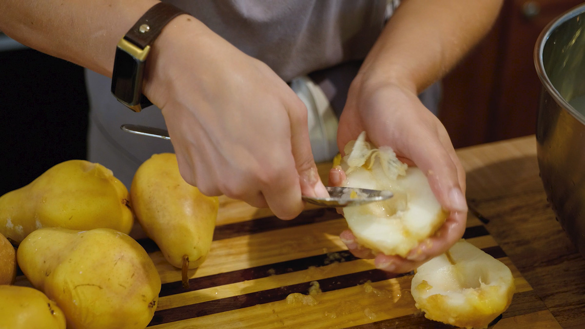 A woman using a spoon to core pears.