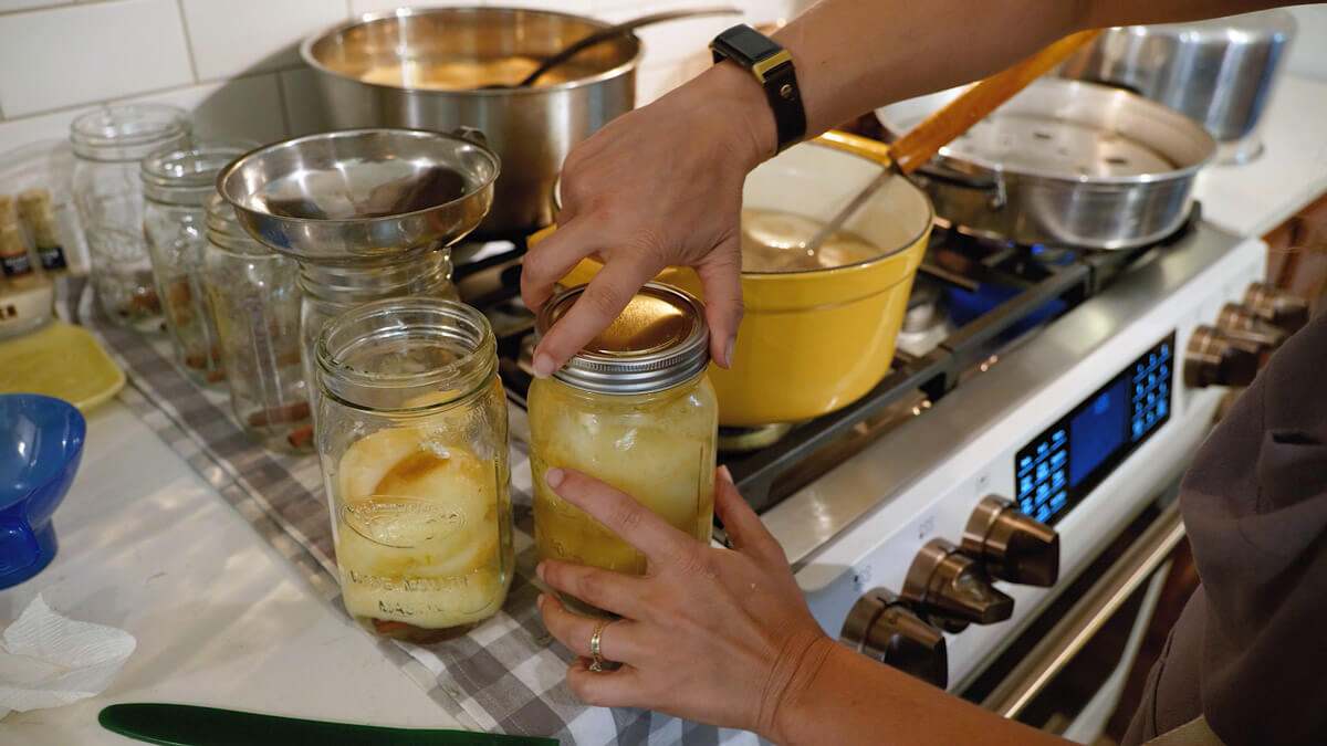 A woman tightening the lid onto a jar of home canned pears.