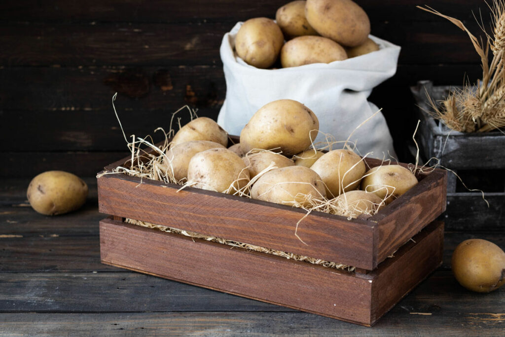 Potatoes stored in a wooden box and a sack.