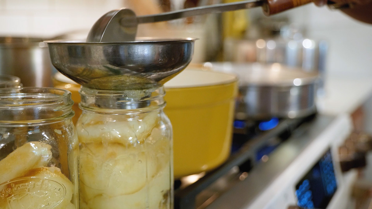 Hot syrup being ladled into a jar of pears.