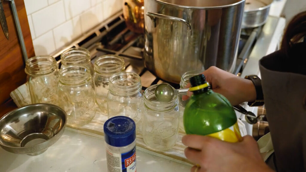 A woman's hands adding lemon juice to canning jars.