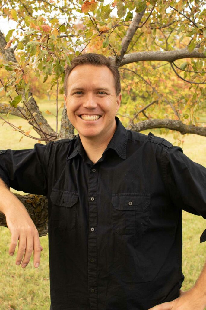 A man standing in front of a tree with fall colors.