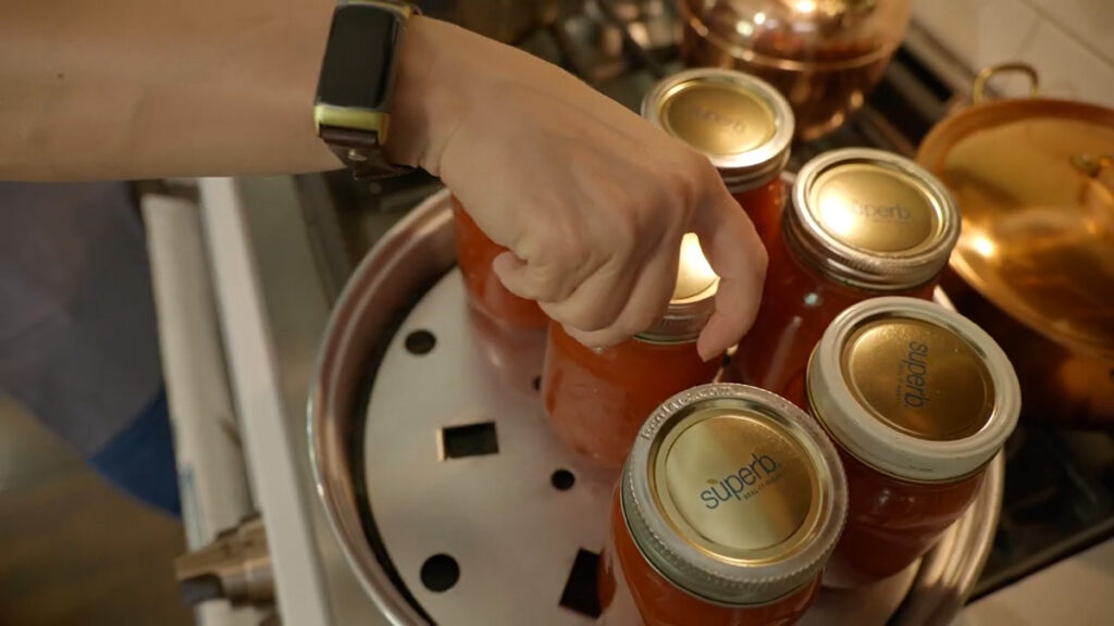 A woman placing jars of tomato sauce into a steam canner.