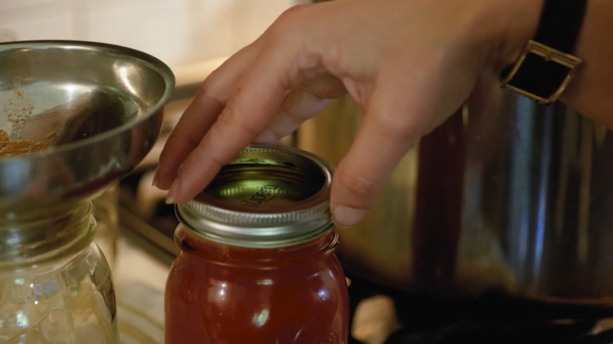 A woman's hand screwing on a canning lid.