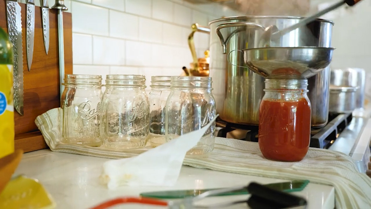 A canning jar being filled with tomato sauce.