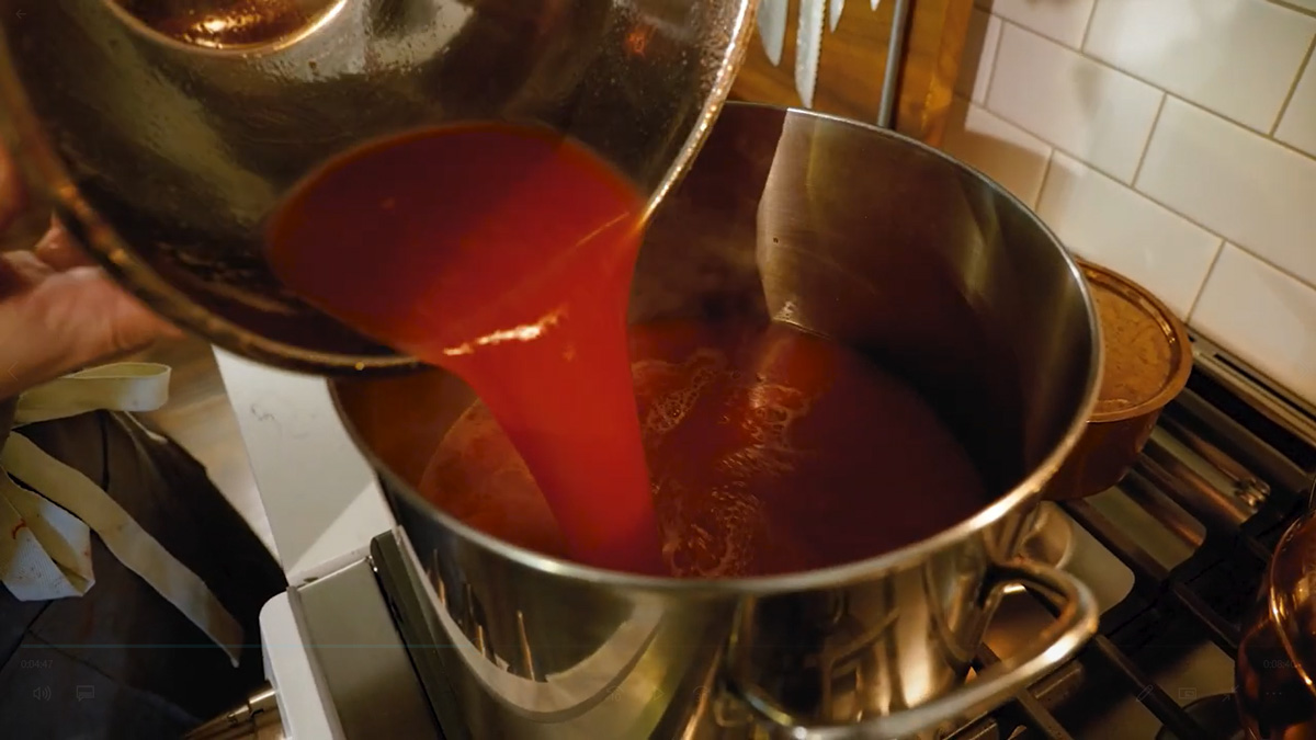 Tomato sauce being poured into a large pot on the stove.